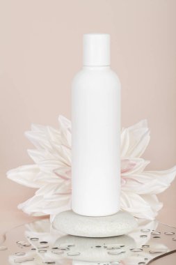 Beyaz çiçekli beyaz şişe losyonu şişesi, bej arka planda taş ve ayna. Doğal organik konsept. Damgalamak ve etiketlemek için şişe.
