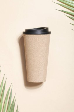 Yeniden kullanılabilir eko kahve ya da bej arka planda palmiye dalı olan çay fincanı. Sürdürülebilir yaşam tarzı. 