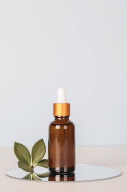 dark amber glass bottle with oil on mirror with green leaf on blue background. copy space. Beauty concept