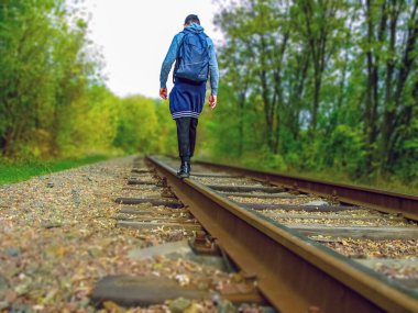 Genç bir adam demiryolu boyunca yürür. Arkadan bak. Yaya olarak aktif eğlence. Vahşi yaşam.