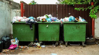 Şehrin sokaklarında taşan çöp tenekeleri. Çöp tenekelerinin yanında yerde yatıyor. Kötü koku etrafa yayılıyor. Çevre kirliliği. Büyük şehirlerin sosyal sorunları.