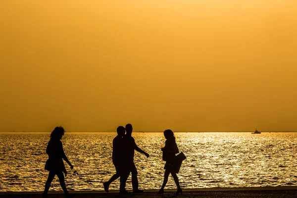 Silhouettes of people enjoying a walk by the seaside of the town — Stock Photo, Image