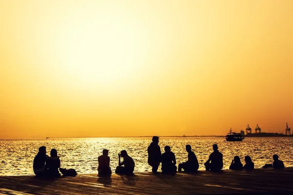 Mensen ontspannen aan de waterkant bij zonsondergang — Stockfoto