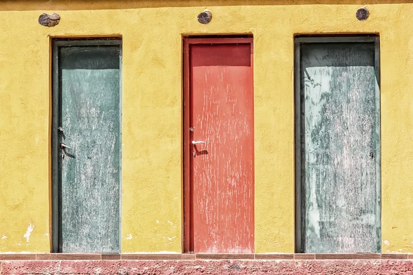 Trzy kolorowe stare drewniane drzwi i żółta ściana — Zdjęcie stockowe