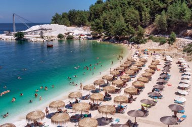 Porto Vathy, Mermer Sahili, Thassos, Yunanistan - 19 Temmuz 2021: Porto Vathy plajının zümrüt ve şeffaf Akdeniz manzaralı plajı, plaj şemsiyeleri ve yüzen turistlerle dolu