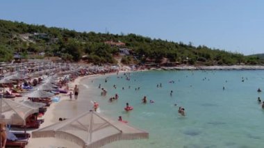Psili Ammos, Thassos Adası, Yunanistan - 17 Temmuz 2021: Yukarıdan bakıldığında, plaj şemsiyeleriyle dolu beyaz bir plaj ve dinlenip yüzen turistlerle dolu bir zümrüt ve şeffaf Akdeniz manzarası. 