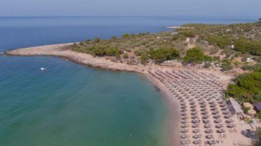Yukarıdan bakıldığında, zümrüt ve şeffaf bir Akdeniz manzarası, plaj şemsiyeleri ve dinlenip yüzen turistlerle dolu beyaz bir plaj. Psili Ammos, Thassos Adası, Yunanistan - 17 Temmuz 2021