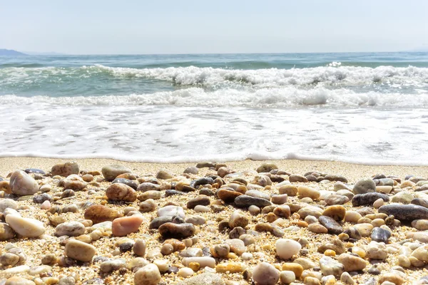 Волна моря на песчаном пляже с морскими камнями спереди — стоковое фото