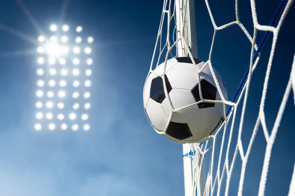 Soccer ball in the goal net with stadium lights in the backgroun — Stock Photo, Image