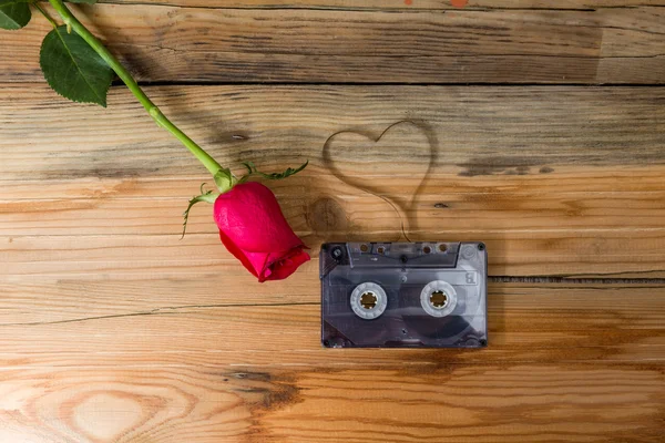 Rose and vintage audio cassette with loose tape shaping one hear — Stock Photo, Image