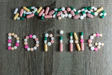 The word doping written with pills on a wooden background.  clipart