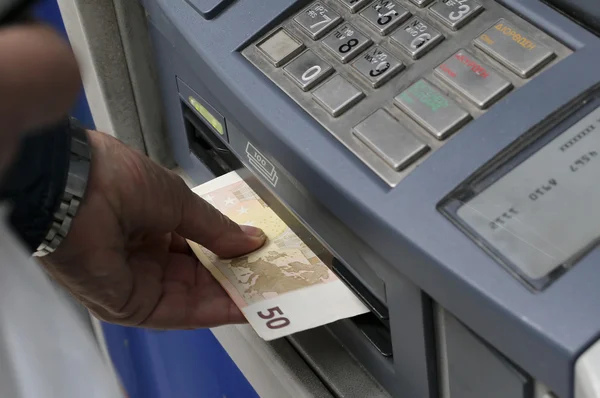 People stand in a queue to use the ATMs of a bank