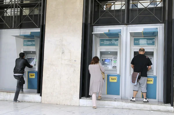 People stand in a queue to use the ATMs of a bank