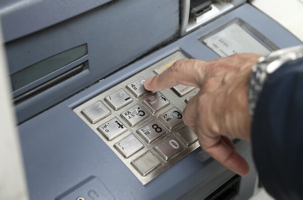 People stand in a queue to use the ATMs of a bank
