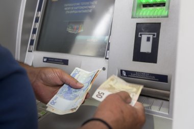 People stand in a queue to use the ATMs of a bank. Person receiv