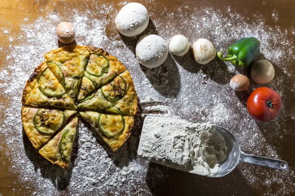 Italian pizza in pieces with flour and ingredients on a wooden t — Stock Photo, Image