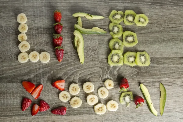 Le mot vie écrit avec des fruits sur un fond de bois . — Photo