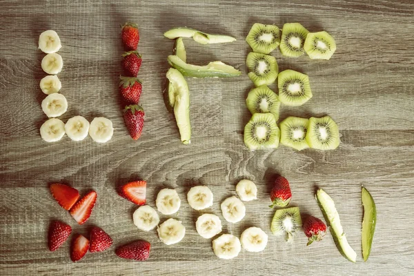 Le mot vie écrit avec des fruits sur un fond de bois . — Photo