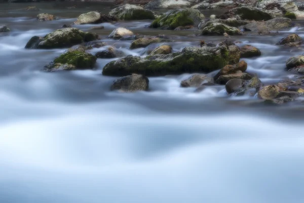 Piedras en un arroyo con agua borrosa por exposición prolongada usando ND — Foto de Stock