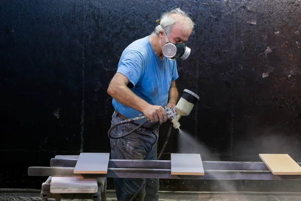 Hombre trabajador pintura tablero de madera con pistola de pulverización usando protecti —  Fotos de Stock