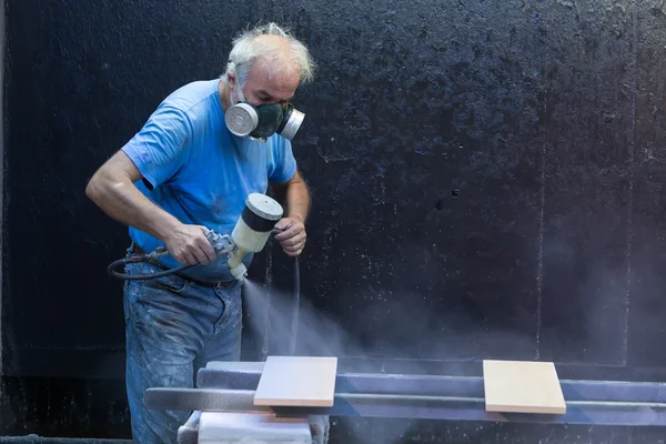 Man werknemer schilderen houten plank met spuitpistool dragen ve — Stockfoto