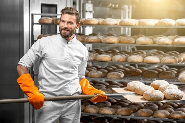 Baker colocando com loafs pão pá na fabricação — Fotografia de Stock