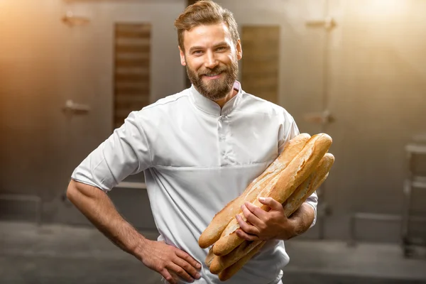 Baker segurando baguetes na fabricação — Fotografia de Stock