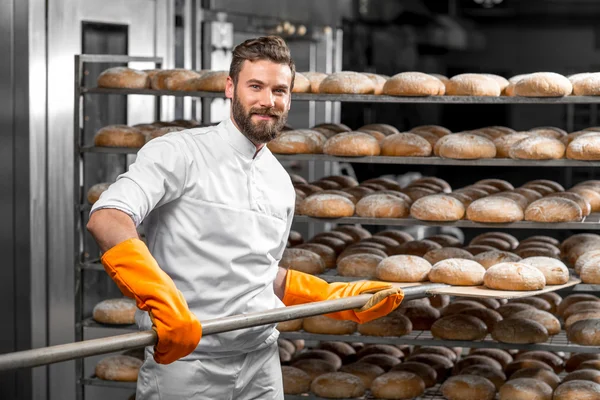 Baker colocando com loafs pão pá na fabricação — Fotografia de Stock