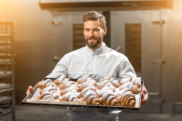 Piekarz przystojny przytrzymanie tacą pełną świeżo pieczone croisants — Zdjęcie stockowe