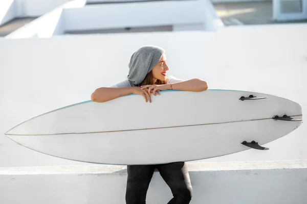 Mulher com prancha de surf no fundo da cidade branca — Fotografia de Stock