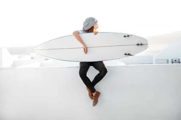 Женщина с доской для серфинга на фоне белого города — стоковое фото