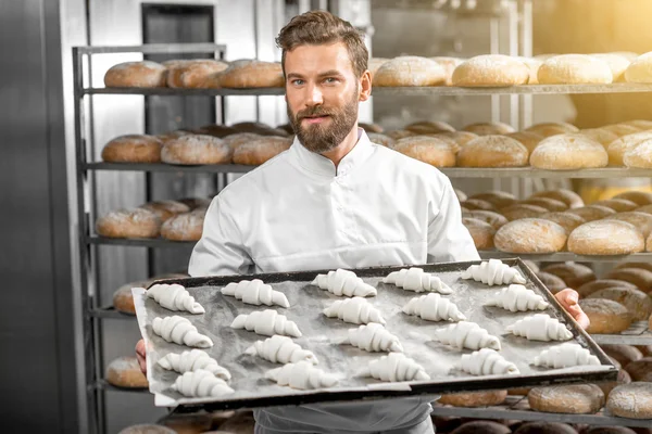 Piekarz przystojny przytrzymanie tacą pełną świeżo pieczone croisants — Zdjęcie stockowe