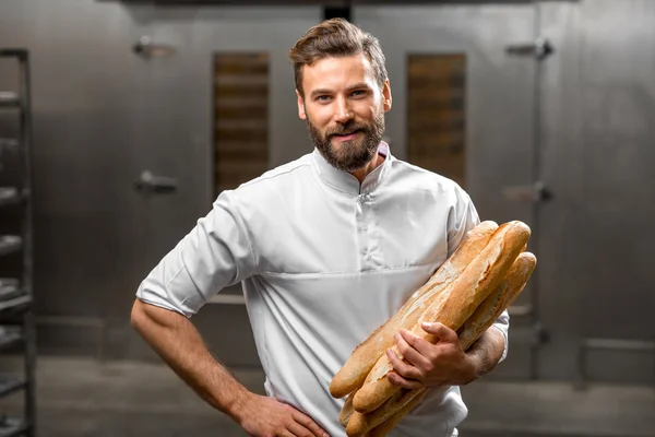Пекарь держит багеты на производстве — стоковое фото