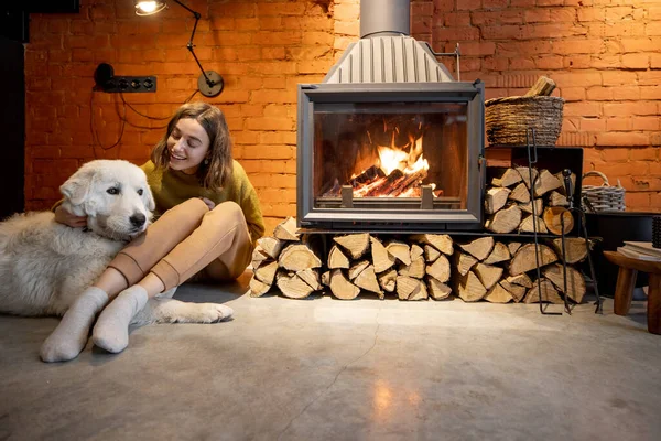Woman by the fireplace with a white dog — Stock Photo, Image