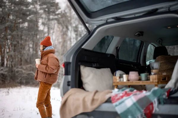 Frau mit Heißgetränk bleibt in der Nähe des Kofferraums im Winterwald — Stockfoto