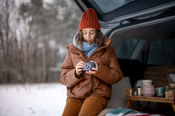 Woman with old camera sitting in car trunk