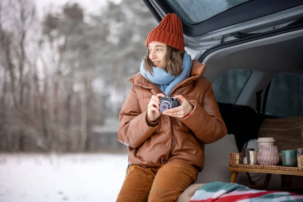 Woman with old camera sitting in car trunk