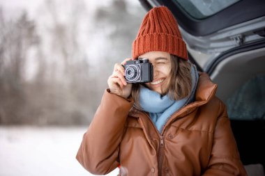 Woman with old camera smiling and sitting in car trunk  clipart