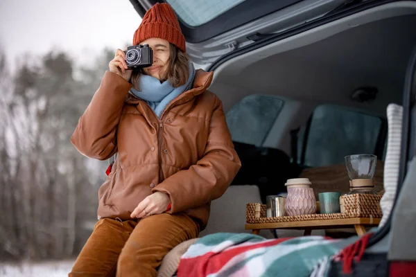 Woman with old camera smiling and sitting in car trunk