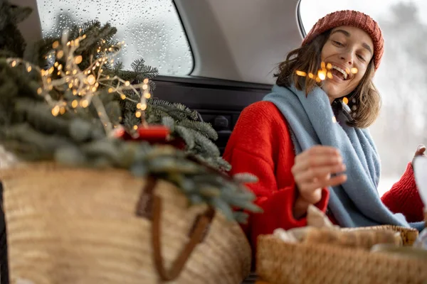 Mulher sorrindo e olhando para sparkler enquanto sentado no porta-malas do carro — Fotografia de Stock