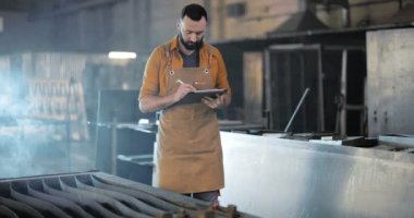 Fabrika işçisi, tablet ve telefonla imalat alanında çalışıyor.