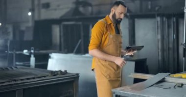 Fabrika işçisi, tablet ve telefonla imalat alanında çalışıyor.