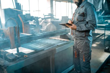 Metal kesme sürecini kontrol eden ağır sanayi işçisi