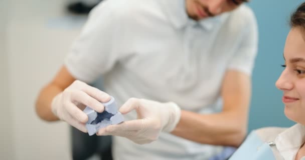 Dentista mostrando modelo de mandíbula para un paciente joven — Vídeo de stock