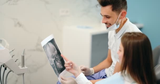 Dentista mostrando radiografía de un cráneo para un paciente joven — Vídeos de Stock