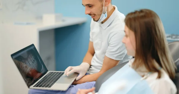 Дантист показывает фотографию зубов на ноутбуке для молодого пациента — стоковое фото