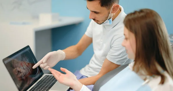 Дантист показывает фотографию зубов на ноутбуке для молодого пациента — стоковое фото