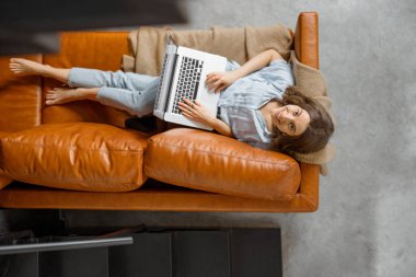 Evden kanepeye dizüstü bilgisayarla çalışan bir kadın.