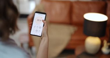 Kadın akıllı bir telefonla oda sıcaklığını ayarlıyor.