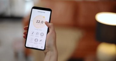 Kadın akıllı bir telefonla oda sıcaklığını ayarlıyor.